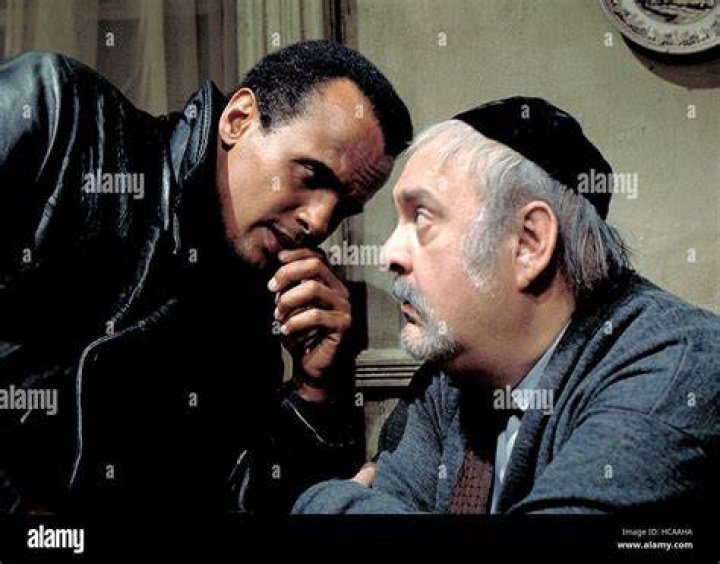 Zero Mostel and Harry Belafonte drink a glass of Passover wine together at a table in a scene from the film 'The Angel Levine,' 1970